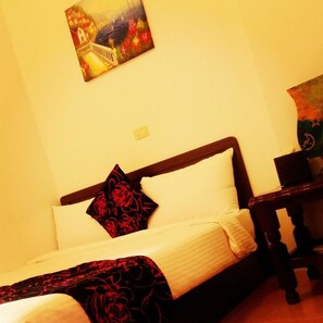 A bed with a white sheet and a black rose-patterned pillow, a wooden headboard, and a painting on the wall. - 179 House (Hengchun)