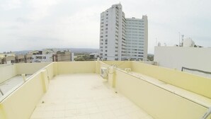 Eine Dachterrasse mit Fliesenboden, geländer und Blick auf ein hohes Gebäude im Hintergrund.