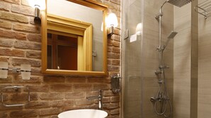 Une salle de bain avec un meuble-lavabo en bois, un grand miroir, une cabine de douche en verre et un mur en briques.