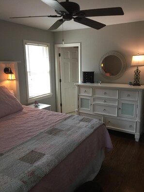 A bedroom with a bed, dresser, ceiling fan, window, and wall-mounted lamp.