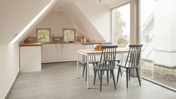 Une cuisine moderne avec des armoires blanches, un comptoir en bois et un coin repas comprenant une table et des chaises. Une fenêtre laisse entrer la lumière naturelle et offre une vue sur l’ext érieur.