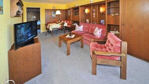 Una sala de estar con televisor, un sofá, una mesa de centro y un comedor con mesa y sillas.