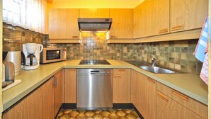 Una cocina con armarios de madera, lavavajillas de acero inoxidable, cafetera y microondas.