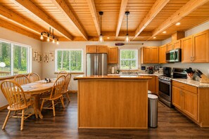 A kitchen with wooden cabinets, a central island, a dining table with chairs, and a large window.