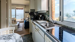 A compact kitchen with a view of the sea, a dining area with a view, and a clock on the wall.