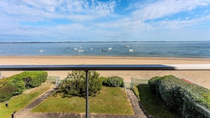 A beach view with boats on the water, a sandy shore, and a pathway leading to the beach.