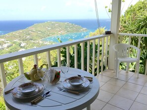 Mesa para dos personas con platos, cubiertos y una copa en un balcón con vista al mar.