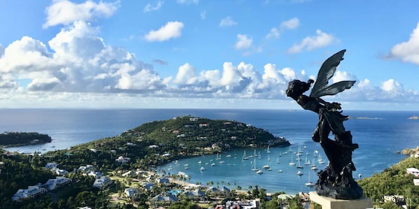 Vista costera con una estatua, una bahía con barcos y una isla densamente poblada.