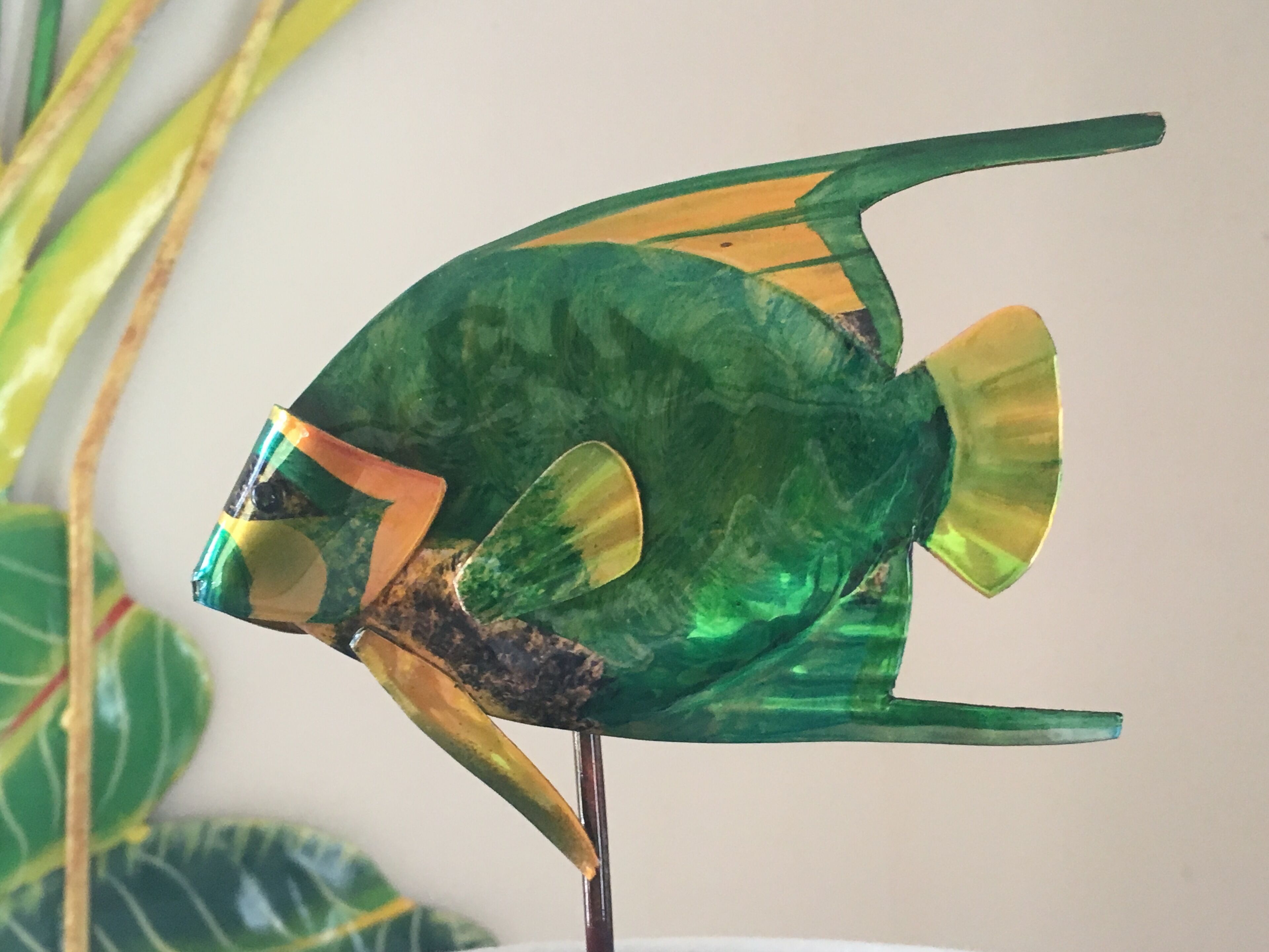 Una scultura di pesce con corpo verde e pinne gialle.