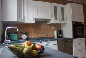 A kitchen with white cabinets, a brick backsplash, a coffee maker, and a fruit bowl on the counter.