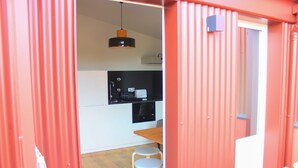 Eine kompakte Küche mit modernen Geräten, ein Essbereich mit Hocker und eine rote Außenfassade.