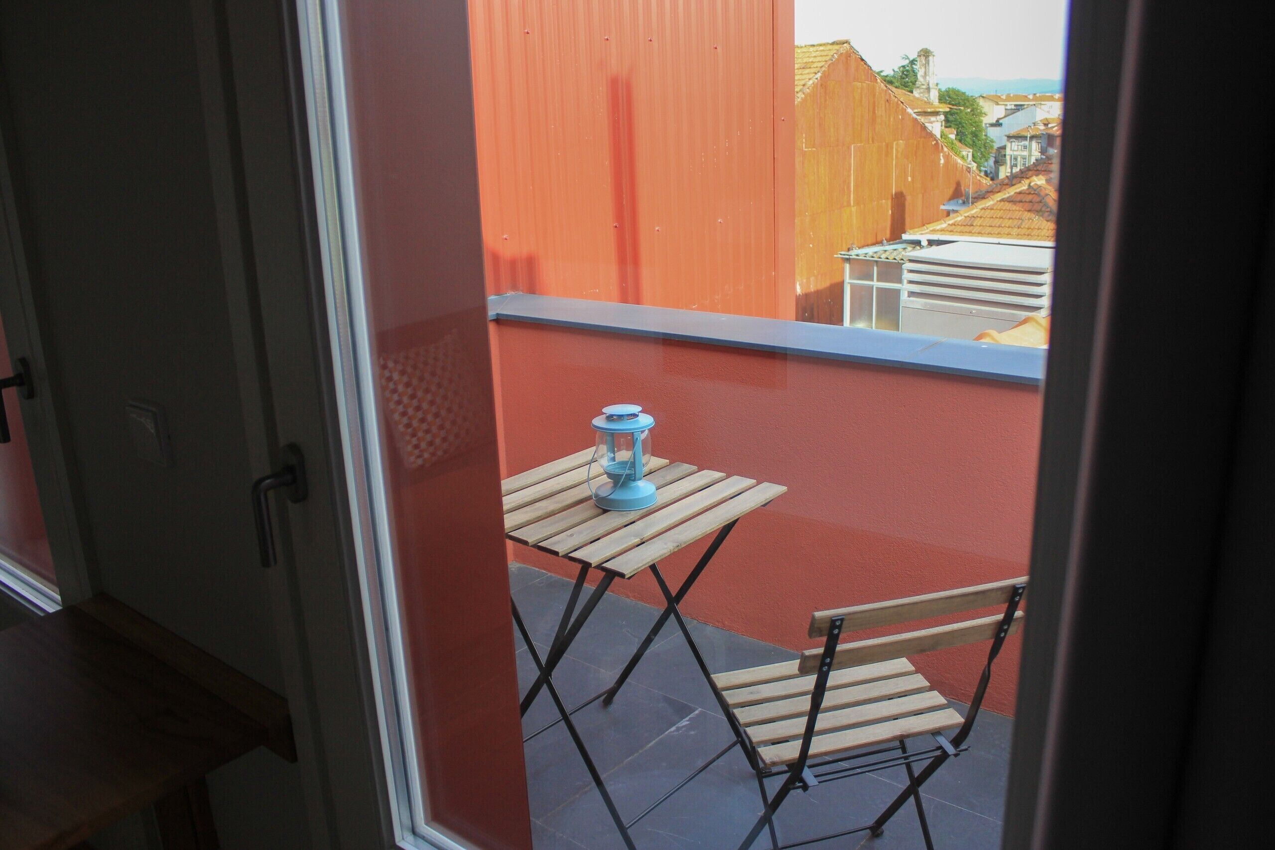A balcony with a wooden table and chair, a blue lantern, and a red wall.