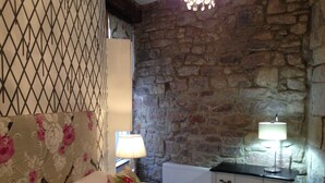 Un dormitorio con pared de piedra, cama con ropa de cama floral, dos lámparas de noche y un radiador.