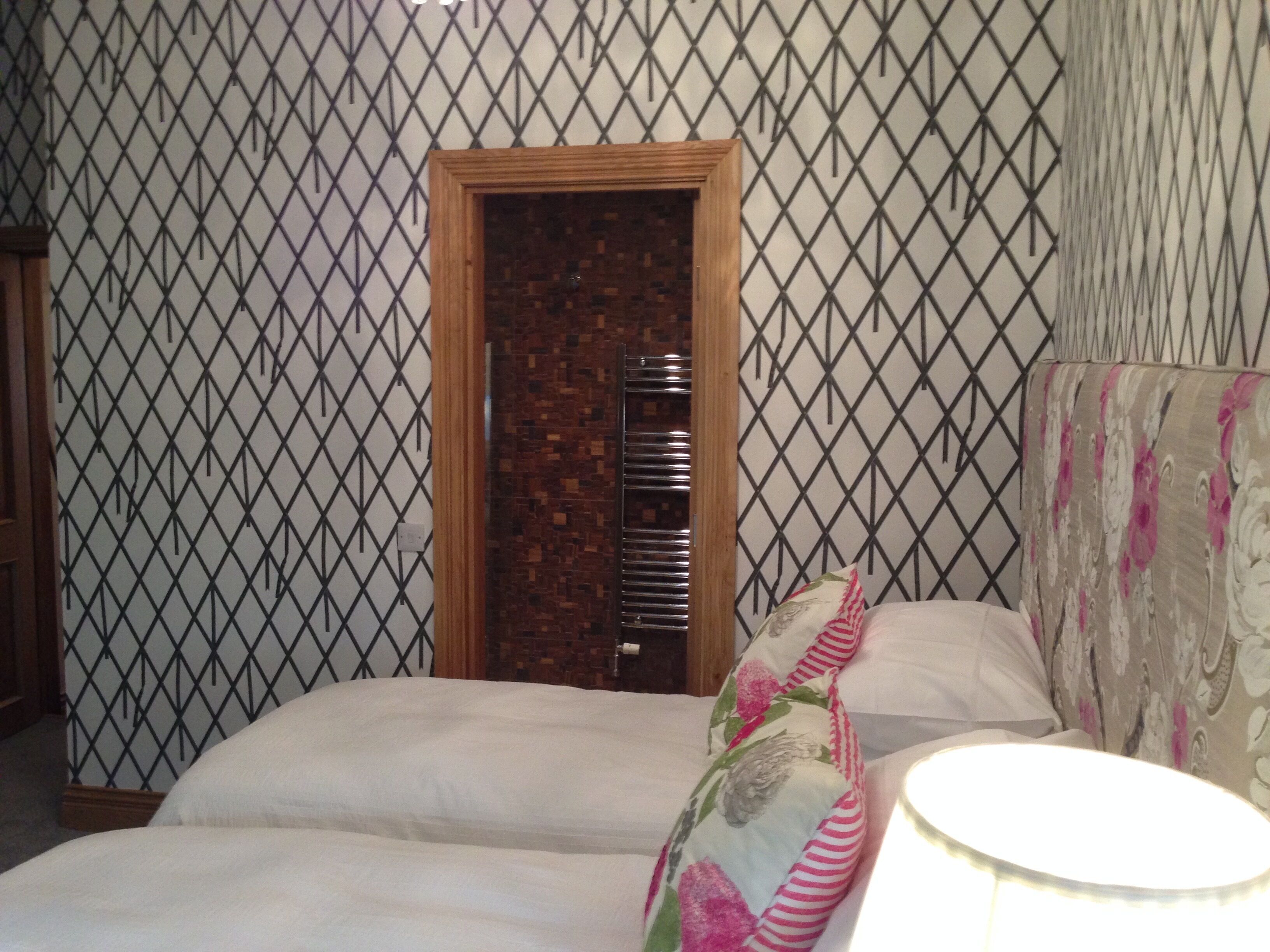 Un dormitorio con cama, mesita de noche, lámpara y pared con diseño.