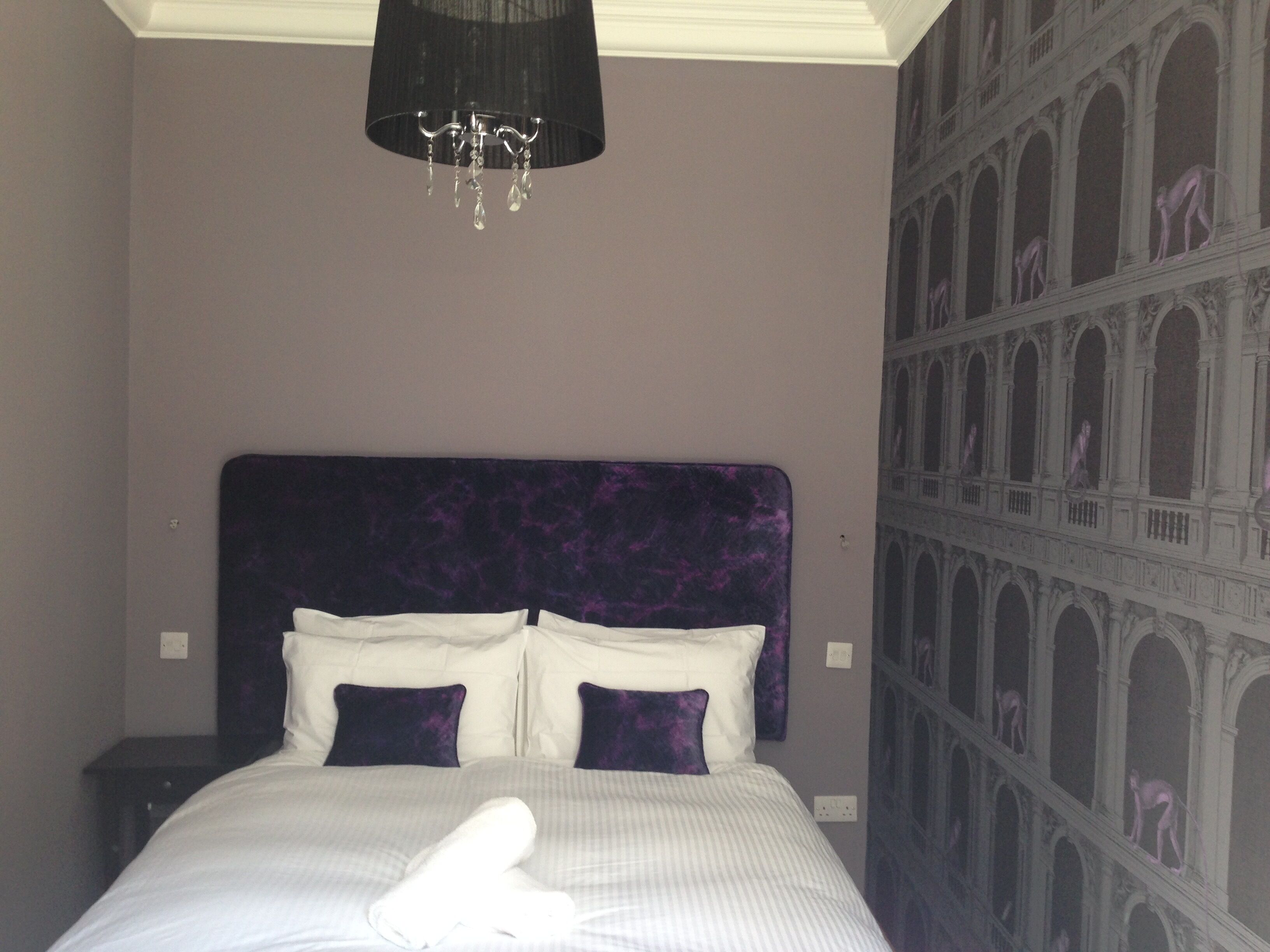 Une chambre à coucher avec un grand lit, un lustre et une fresque représentant un bâtiment classique sur le mur.