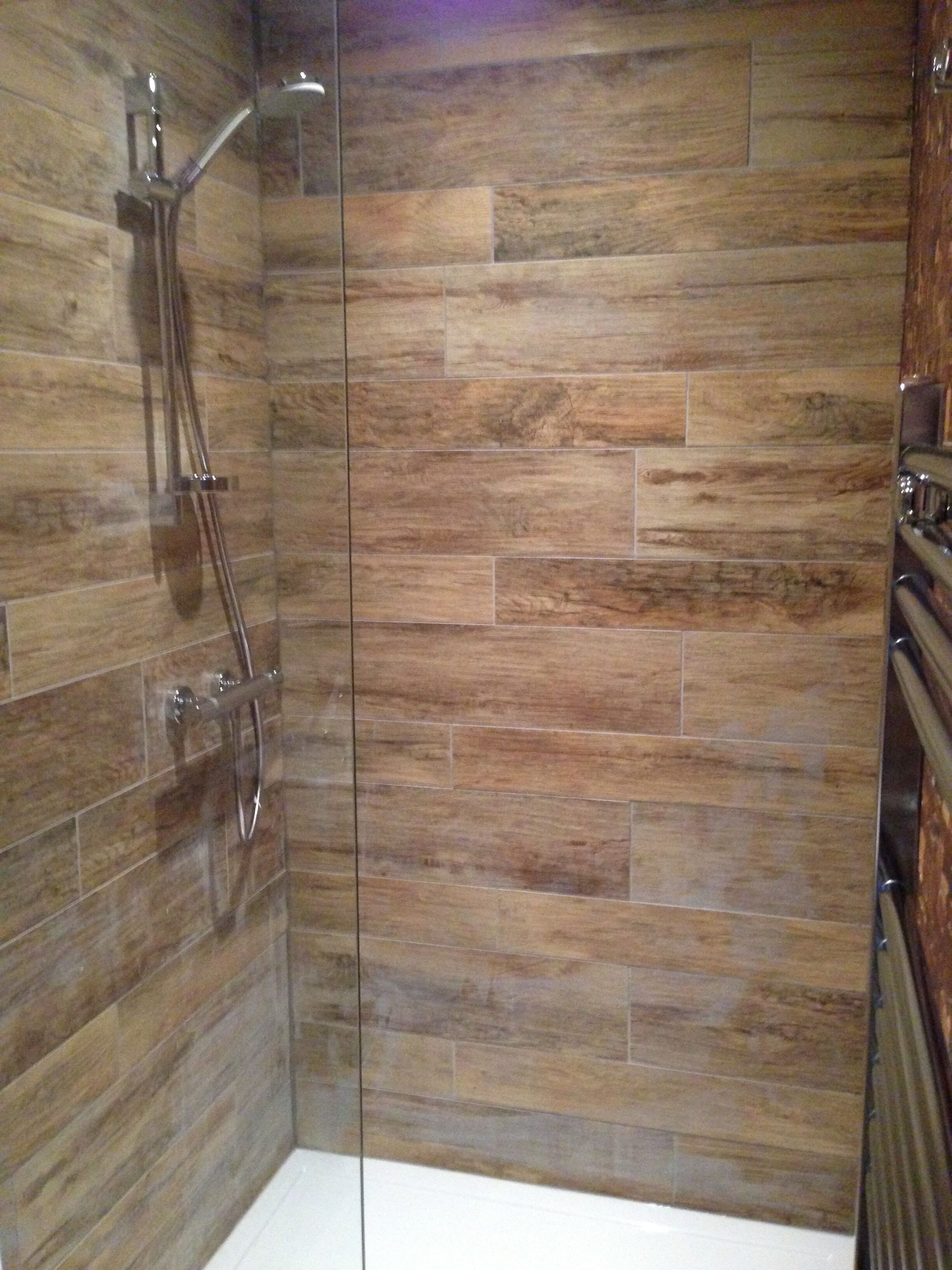 A shower with a glass door and a wooden wall.