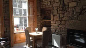Una habitación acogedora con pared de piedra, chimenea, televisor y comedor con sillas y mesa.