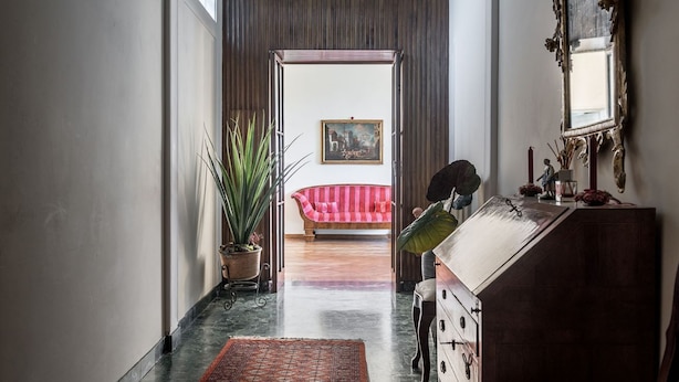Un couloir avec un plancher en bois, une plante en pot, un canapé à rayures rouges et un miroir au mur.