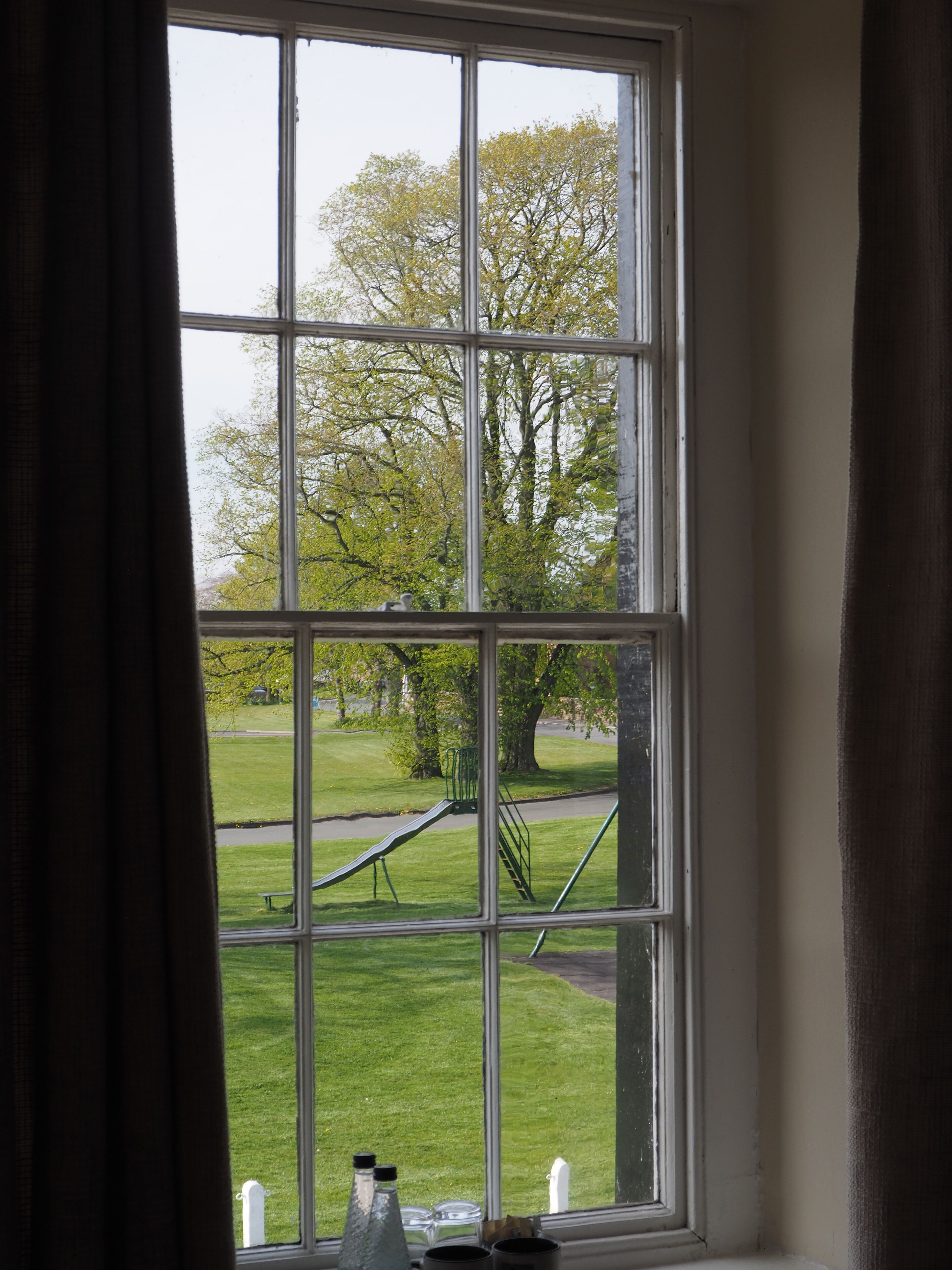 A window with a view of a park, including a playground and trees.