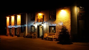 A building with a stone facade, multiple windows, and a door. There are outdoor seating areas with benches and a small Christmas tree. - The Shepherds Inn (Penrith)
