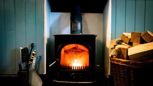 A wood-burning stove with logs and a basket of firewood nearby. - The Shepherds Inn (Penrith)