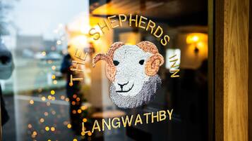 Una ventana con el logotipo de 'The Shepherds Inn Langwathby' y un paisaje urbano borroso al fondo.