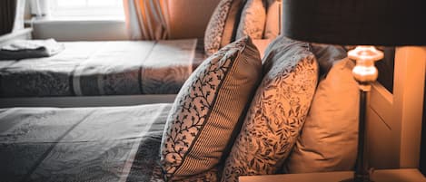 A hotel room with a bed, pillows, a nightstand, and a lamp.