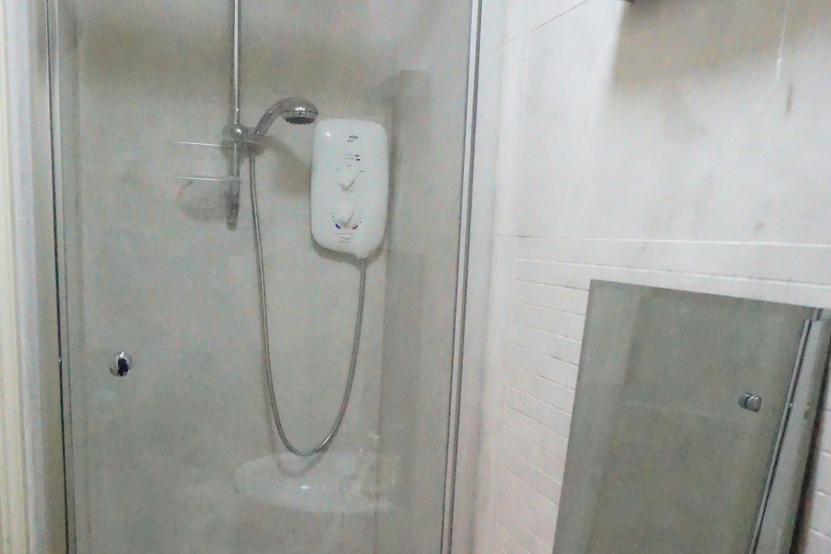 Un baño con ducha de vidrio, un lavamanos blanco con espejo y dispensador de jabón.