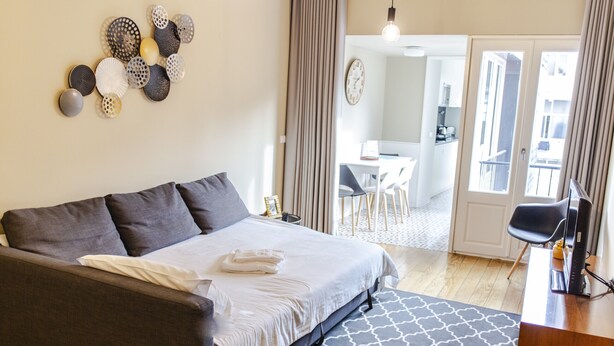 A modern hotel room with a large bed, a desk, and a view of the dining area.