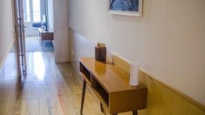 A hotel hallway with a wooden bench, a small table with a vase and a cup, and a framed picture on the wall.