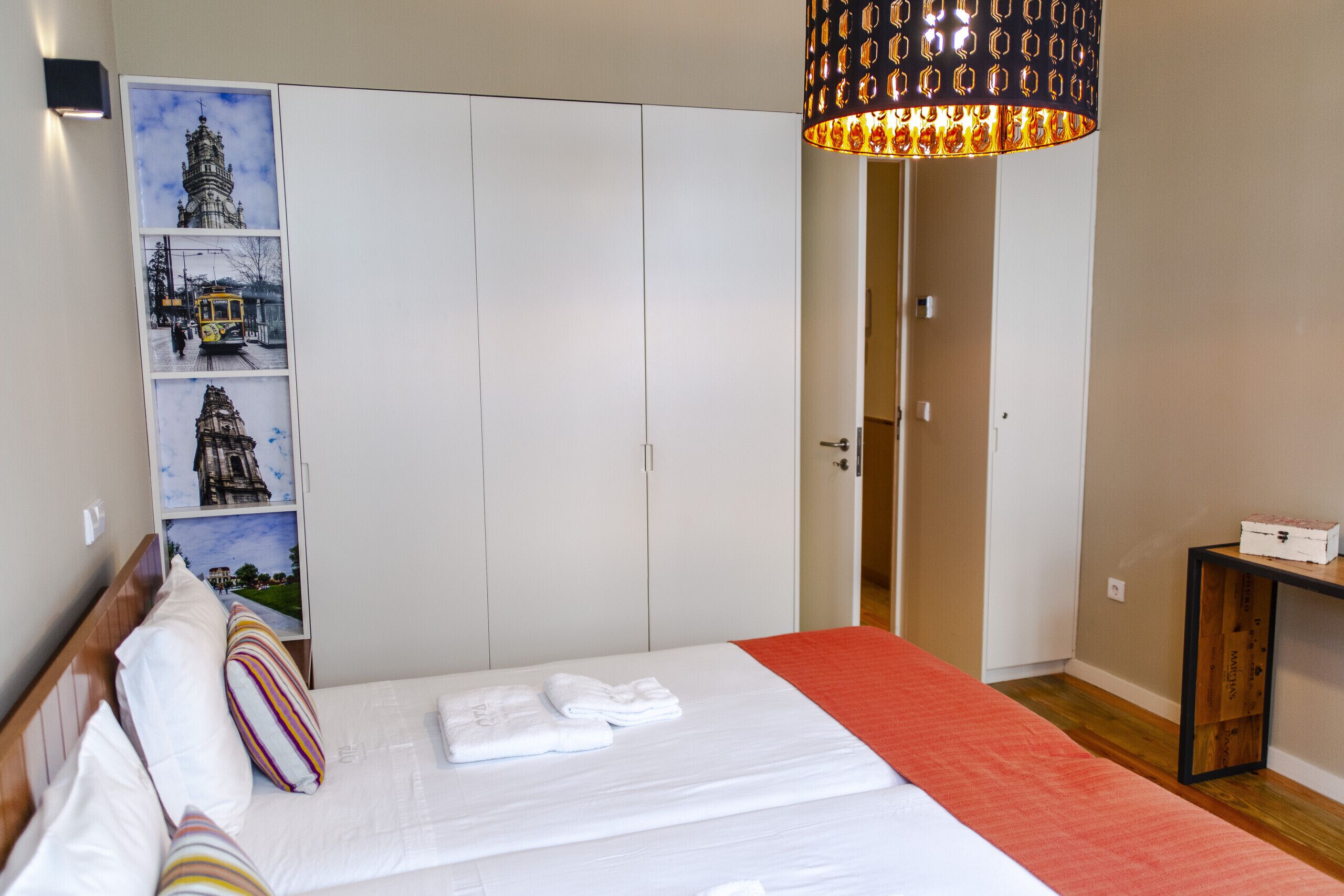 Ein Hotelzimmer mit Bett, weißem Wandschrank, roter Decke, Holzboden und einer Wand mit gerahmten Bildern.