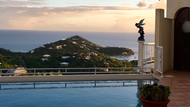 Ein Pool mit Blick auf eine Küstenlandschaft, darunter ein Hügel mit Gebäuden und einer Statue.