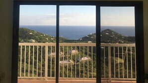 Ein Zimmer mit einer großen Schiebeglasdoor, die auf einen Balkon mit Blick auf das Meer und die Hügel führt.