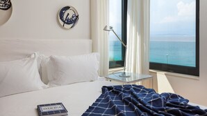 Una habitación de hotel con cama, lámpara de noche, vista al mar y un libro sobre la cama.