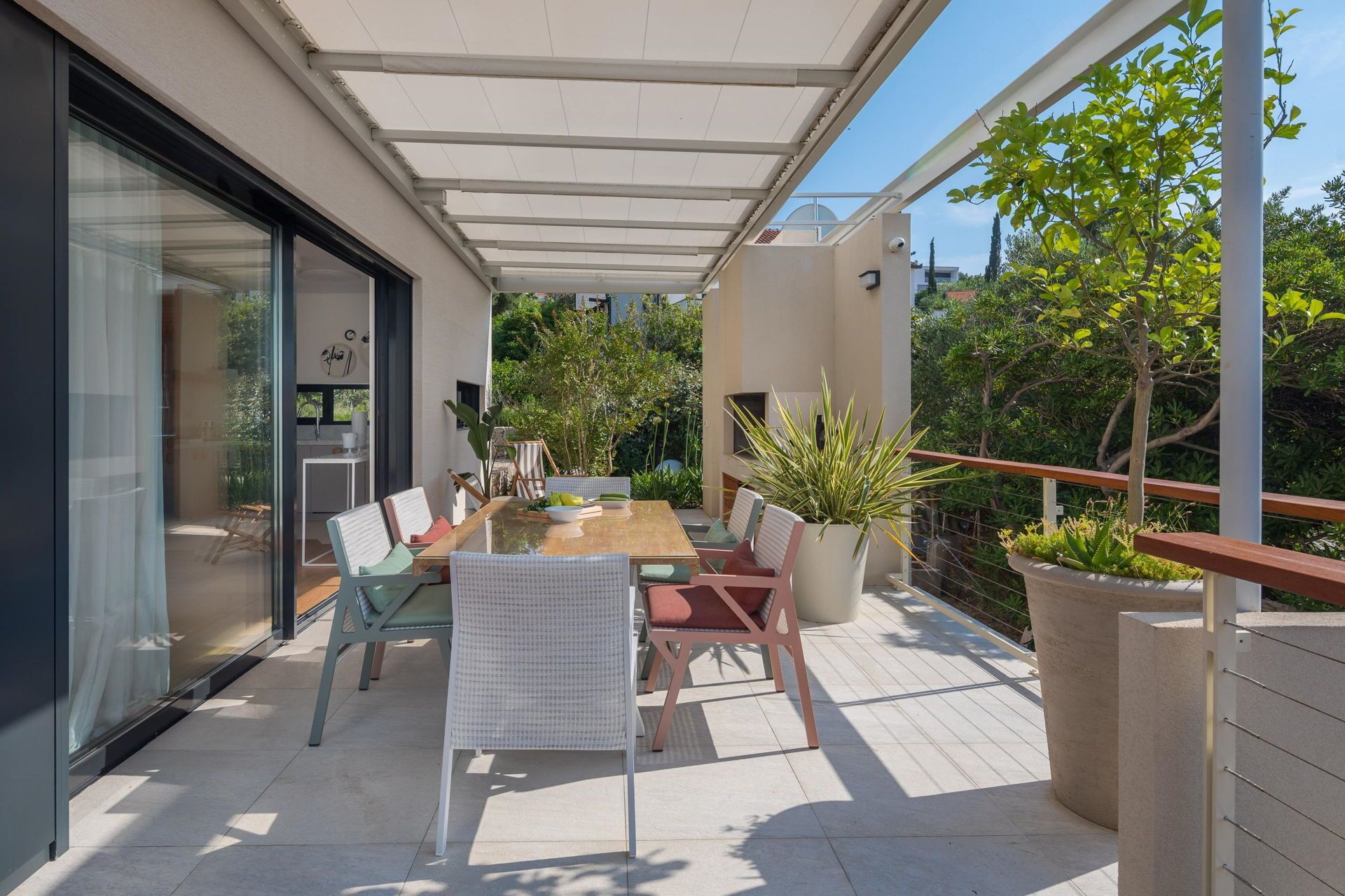 A modern outdoor dining area with a glass enclosure, a wooden table, and comfortable seating.