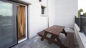 A wooden picnic table on a balcony with a glass door and a small window.
