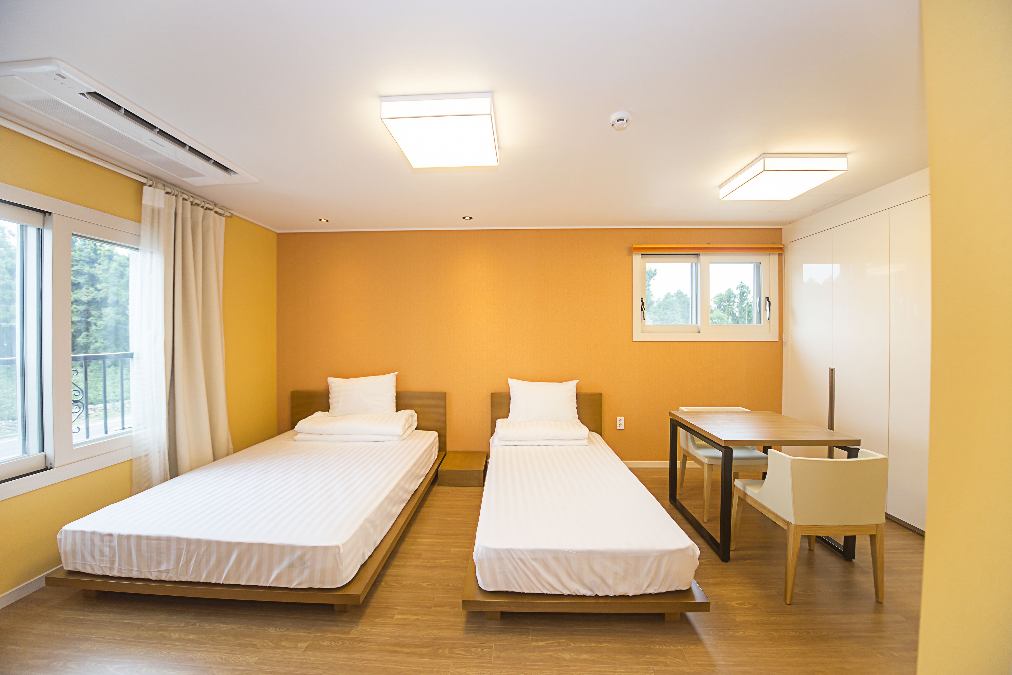 A hotel room with two single beds, a desk with a chair, and a window with curtains.