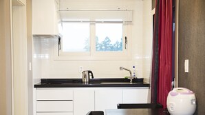 A compact kitchen with white cabinets, a black countertop, a kettle, a toaster, and a window with blinds.