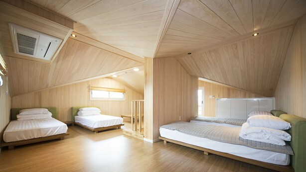 A spacious attic bedroom with wooden floors and sloped ceilings, featuring two single beds and a larger bed.
