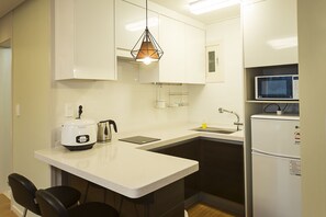 A compact kitchen with a white countertop, a built-in microwave, a refrigerator, a sink, and a hanging pendant light. - Eunbille (Seogwipo)