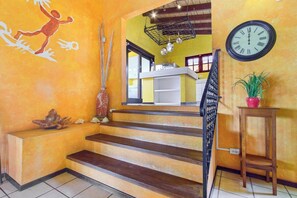 Un escalier menant à un deuxième étage, avec une horloge au mur et une plante posée sur une table d’appoint.