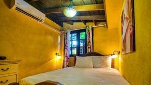 Una habitación con una cama, lámparas de noche, un equipo de aire acondicionado y una ventana con cortinas.