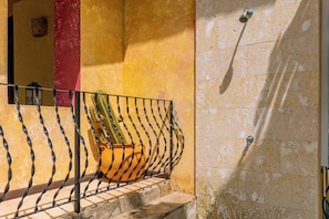 A balcony with a metal railing, a potted plant, and a wall with a water spout.