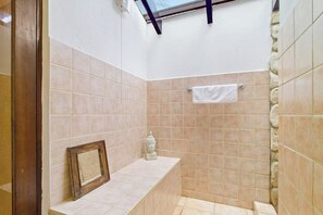 Ein kleines Badezimmer mit beigen Fliesen, einer Duschkabine, einem Handtuchhalter und einem Bilderrahmen an der Wand.