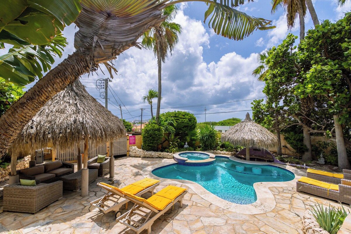 A pool area with lounge chairs, a hot tub, and thatched umbrellas.