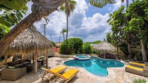 Un área de piscina con sillones de descanso, jacuzzi y sombrillas de paja.