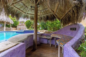Un espace piscine doté d’un toit de chaume, d’un jacuzzi et d’un coin salon avec une table en mosaïque.