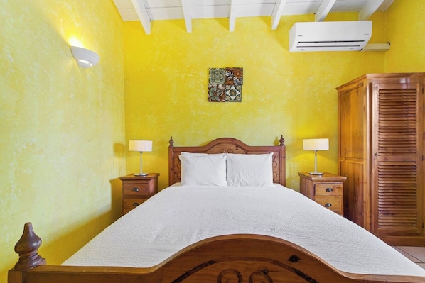 A room with a bed, two bedside tables, a wardrobe, and an air conditioning unit.