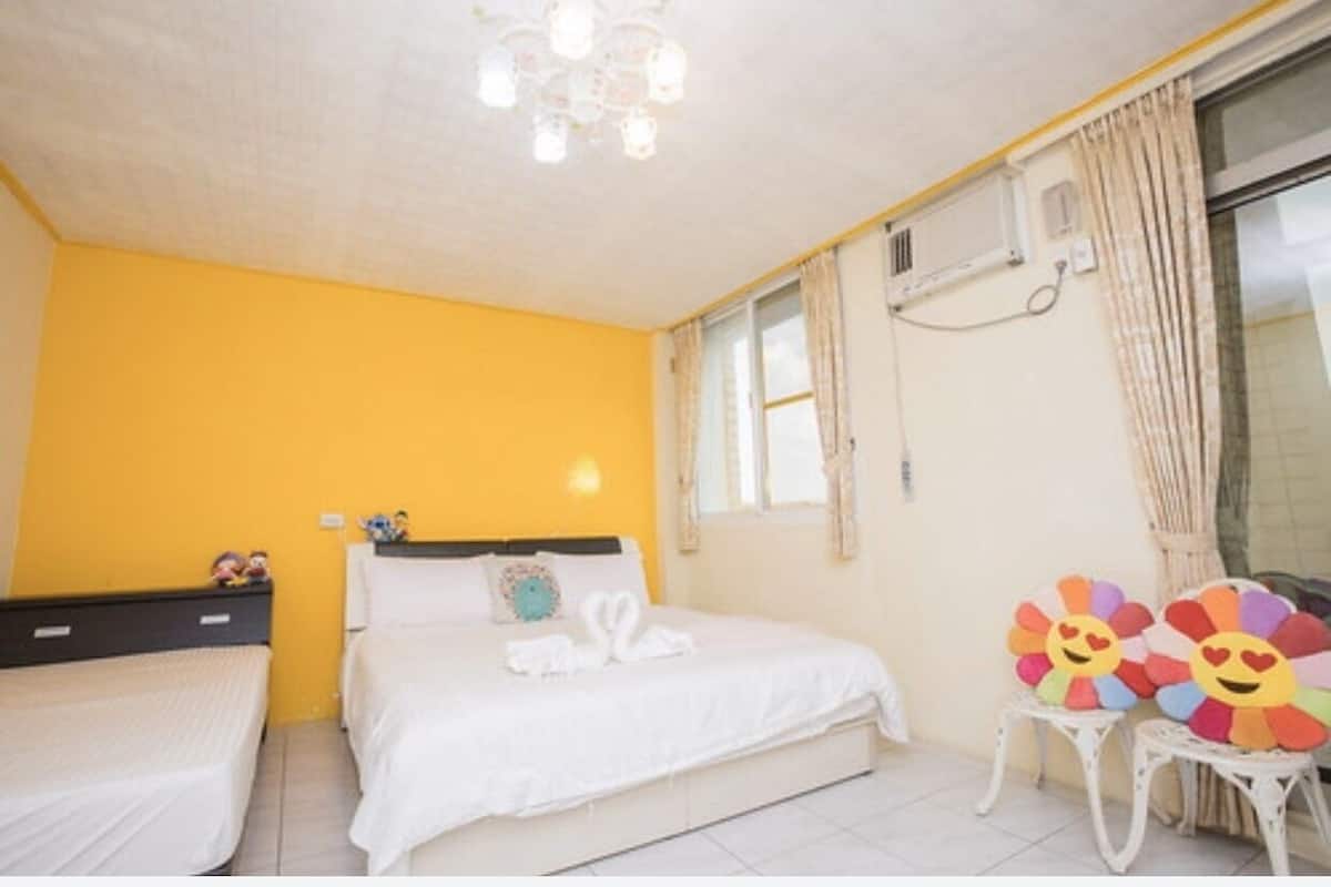 A room with two beds, a window with curtains, a ceiling light fixture, and a wall-mounted air conditioning unit.