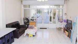 A spacious room with a black leather sofa, a small table with a lace tablecloth, a television, and a cabinet.